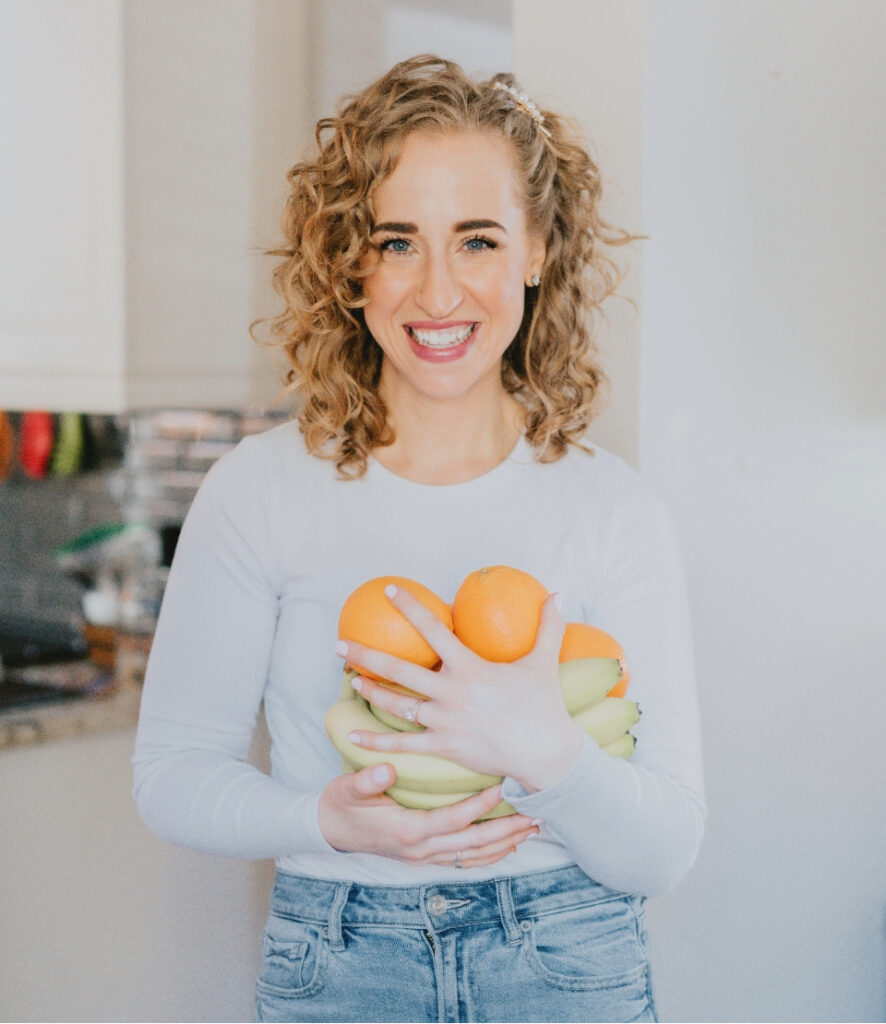 Smiling Danni Smith holding oranges and bananas symbolizing nutrition coaching and wellness