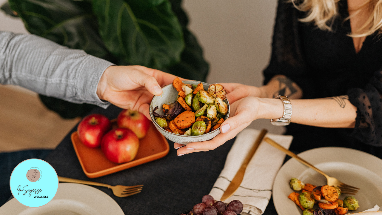 Hands sharing a bowl of roasted vegetables during a mindful meal guided by a Wellness Coach.