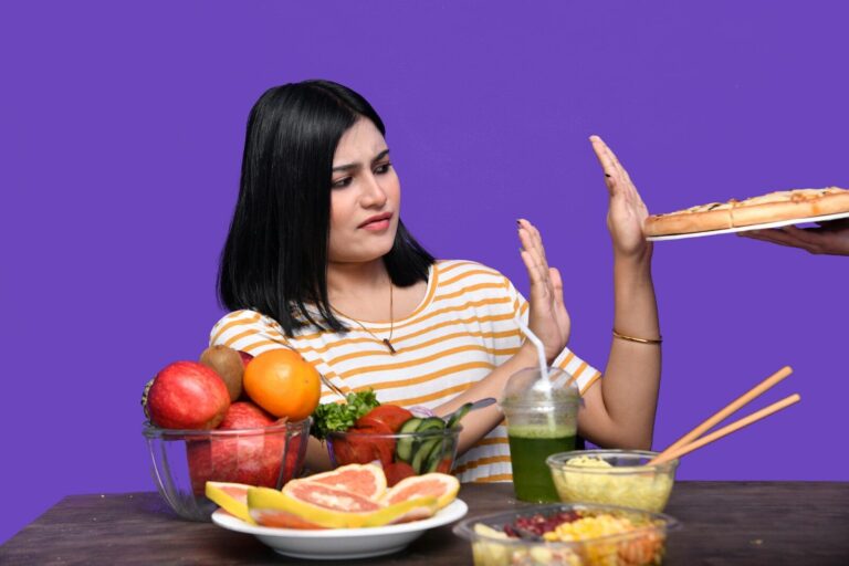 a woman sitting at a table with food and a bowl of fruit