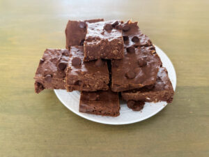Stack of fudgy chocolate brownies with chocolate chips on a white plate.