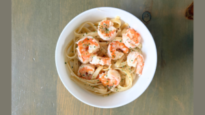 Linguine with shrimp and chopped parsley in a white bowl on a wooden table.