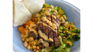 Sliced beef steak with a creamy sauce over broccoli and chickpeas on a blue plate with flatbread nearby.