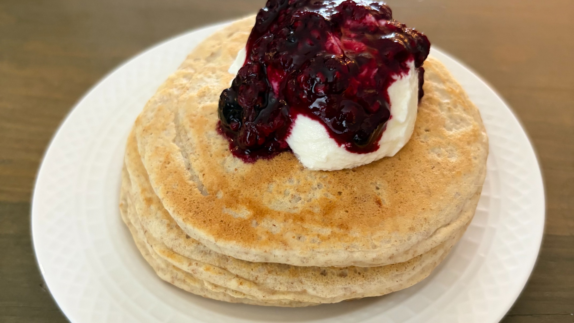Stack of fluffy pancakes topped with berry compote and a dollop of whipped cream on a white plate.