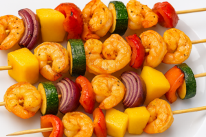 Shrimp and vegetable skewers with shrimp, pineapple, bell pepper, onion, and zucchini on a white plate (grilled).