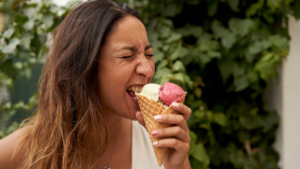 Woman taking a bite of a two-scoop ice cream cone outdoors (vanilla and strawberry).