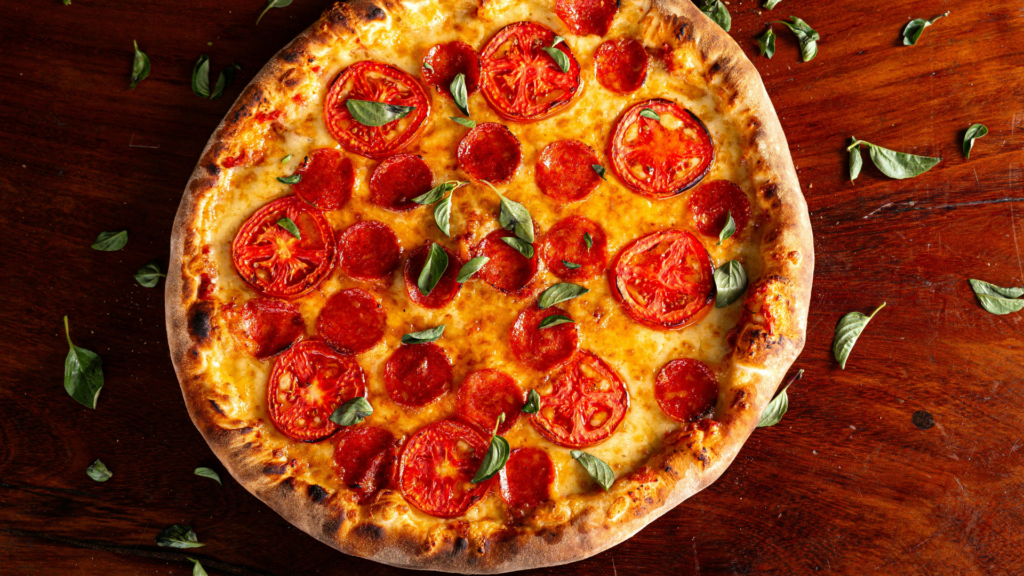 Pepperoni pizza with fresh basil on a wooden tabletop.