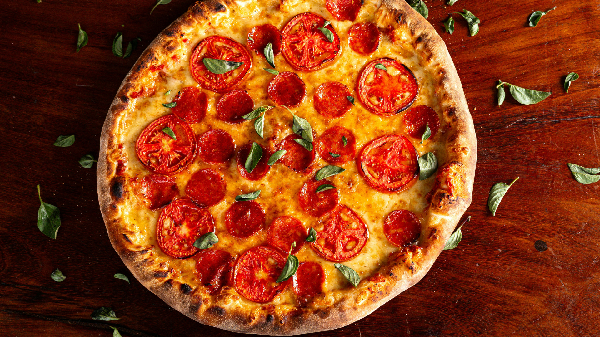 Pepperoni pizza with fresh basil on a wooden tabletop.